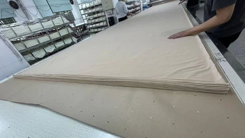Factory workers preparing layers of fabric on an automated cutting table before lingerie production.